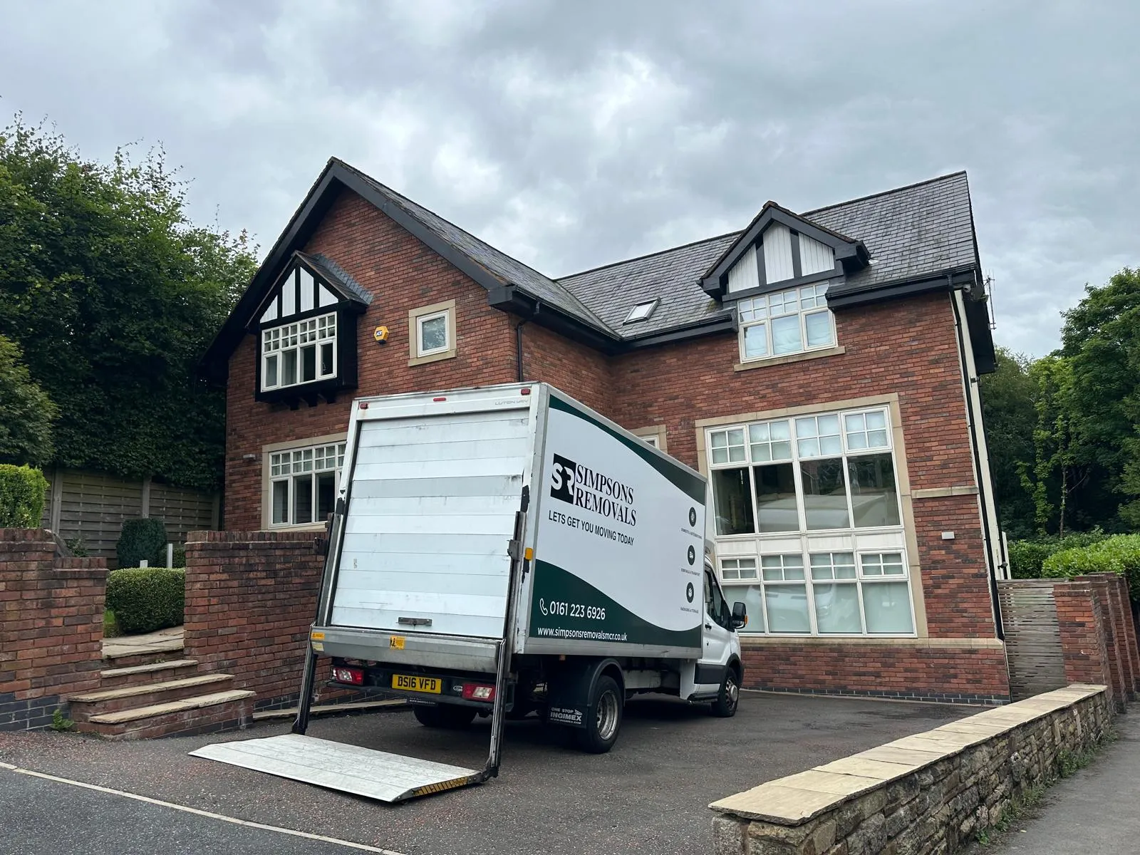 Simpsons Removals van with ramp down outside a large detached house